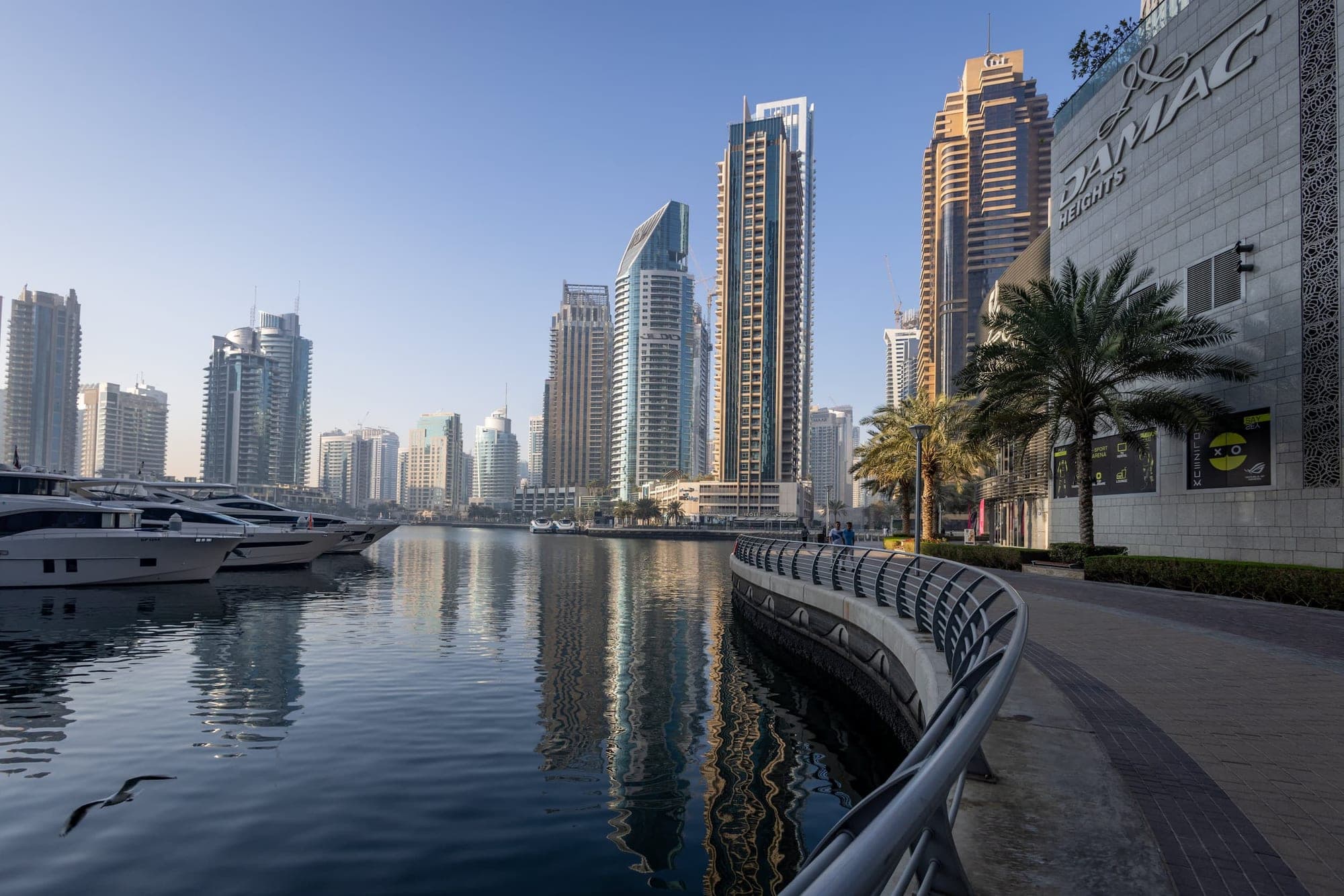 A Dubai Marina sétánya és felhőkarcolói reggeli fényben, jachtokkal a kikötőben.